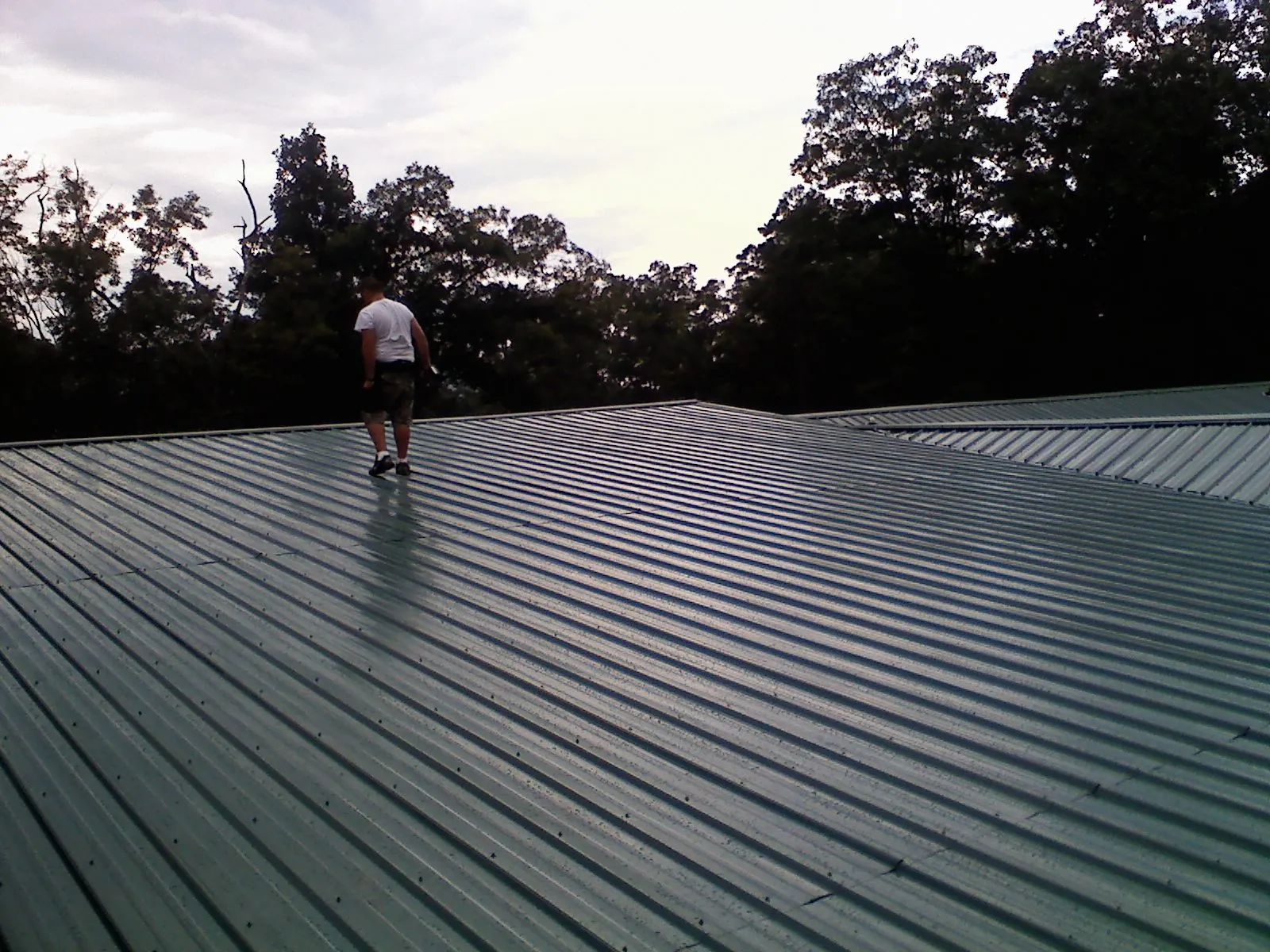 Roofer walking a wide expanse of new green metal roofing in Terryville