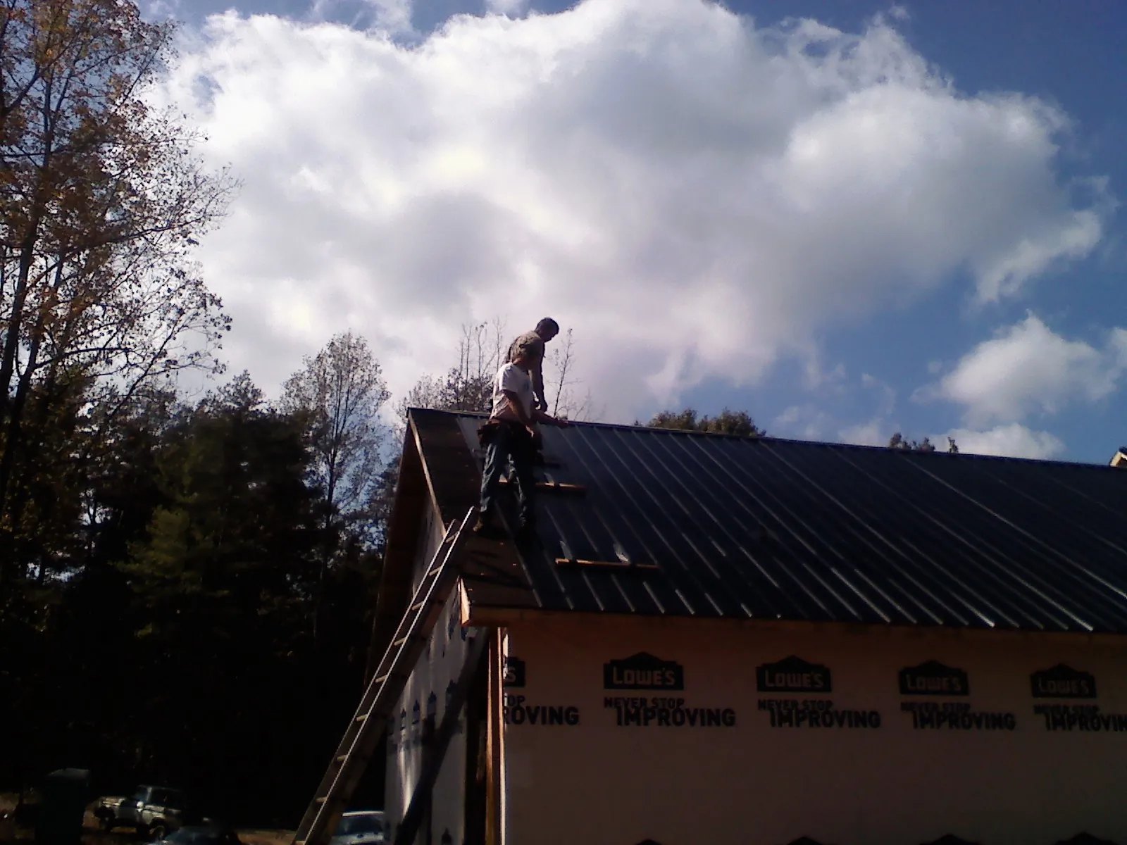 Roofer fastening dark metal panels high against a cloudy sky, from a Roof Inspection job in Terryville