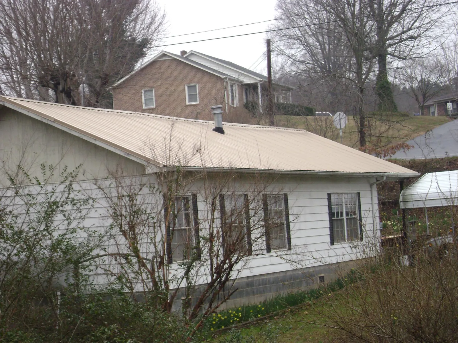 Tan metal roof on a white sided house set into a hillside — Commercial Roofing by Roofing Brothers in Terryville