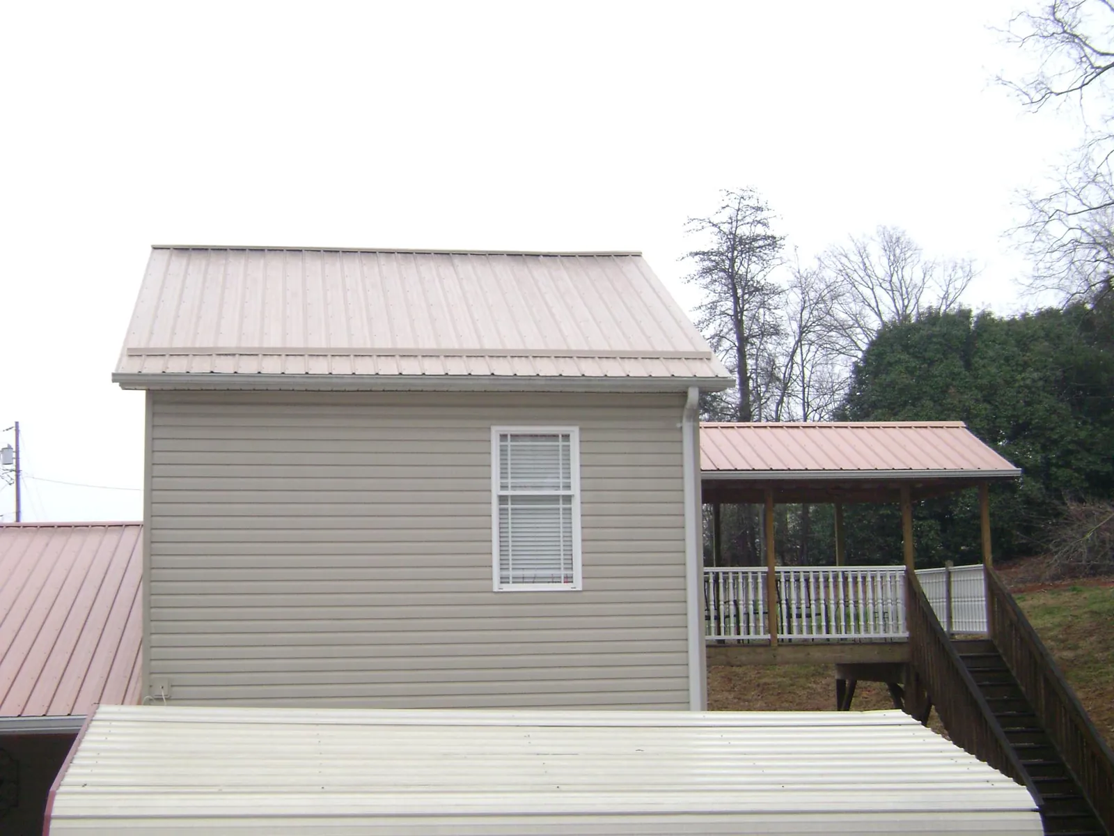 Tan metal roofs on a two story addition and attached porch, from a Roof Replacement job in Terryville
